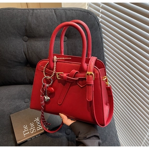 Dettaglio della borsa da sposa rossa con ciondoli a cuore e tracolla su un divano grigio