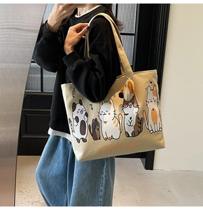 Detail view of large beige canvas tote bag with cute cartoon cats and plush dog charm