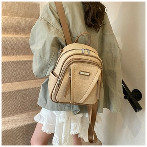 Detail of beige straw texture backpack with brown leather straps and metal logo plate