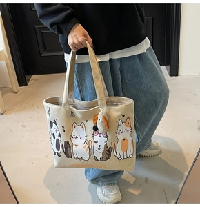 Detailed view of beige canvas tote bag with cat prints and a plush dog charm attached