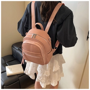Rear view of model wearing pink mini leather backpack with zipper pockets and slim straps