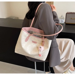 Detail of white tote bag featuring embossed lucky patterns and pink plush pendant