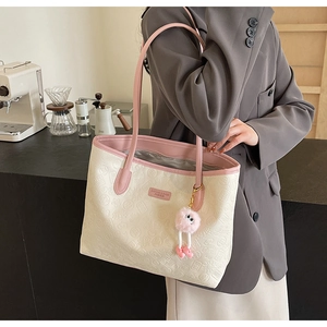 Pink and beige embossed tote bag with pompom charm shown on shoulder with grey blazer