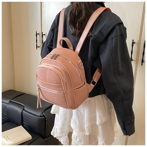 Detail of pink faux leather mini backpack showing textured finish and zipper compartments