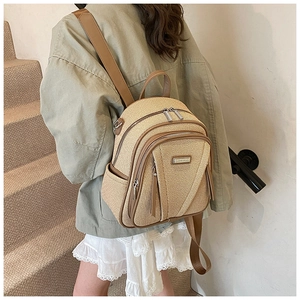 Rear view of a woven straw backpack with brown leather straps worn on model's back