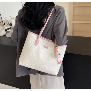 Detail of white embossed tote bag with pink straps and a plush charm on a model