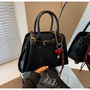 Dettaglio di una borsa in pelle nera con ciondolo a cuore e hardware dorato