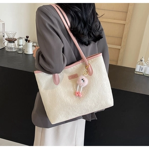 Detail of cream tote bag with pink straps and embossed patterns with plush charm