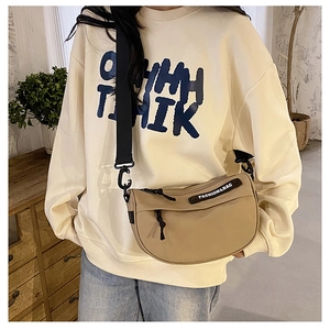 Detail of khaki nylon crescent bag with wide black strap and fashion label on shoulder
