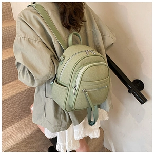Mini sage green backpack with textured fabric and multiple pockets shown on model