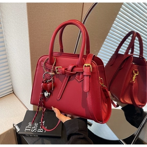 Dettaglio borsa da sposa in pelle rossa con ciondolo a cuore e tracolla intrecciata