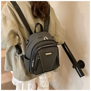 Detail of grey fabric mini backpack with black leather trim and metal plate on back