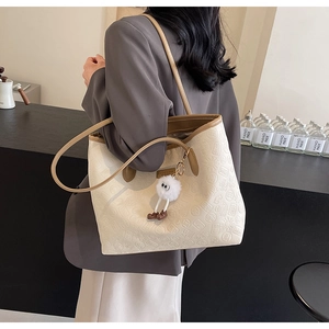 Detail of cream tote bag featuring embossed patterns and a plush doll pendant