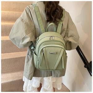 Detailed close-up of mint green fabric backpack with metal logo and zipper texture