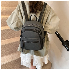 Rear view of a dark grey multi-zipper backpack worn with casual clothing for women