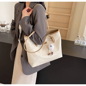 Detail of cream tote bag with embossed vintage patterns and plush charm on brown handles