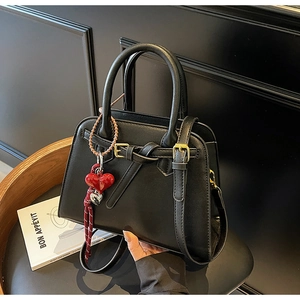Dettaglio di una borsa nera opaca con ciondolo a cuore rosso su una sedia di legno