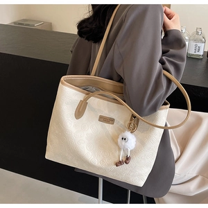 Detail of embossed floral patterns and metal brand plate on large beige tote bag