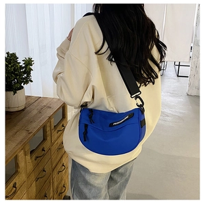 Blue nylon saddle crossbody bag with wide strap worn by a model in a minimalist studio