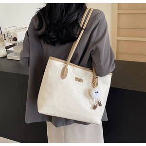Detail of white embossed tote bag with brown straps and cute plush pendant charm