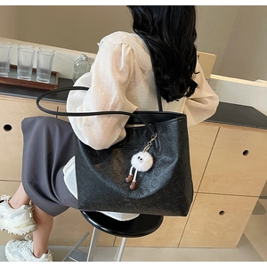 Detail of black embossed tote bag with a cute white plush charm on a long shoulder strap