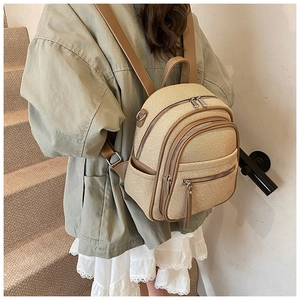Detail of woven straw backpack featuring brown leather trim and triple zipper pockets
