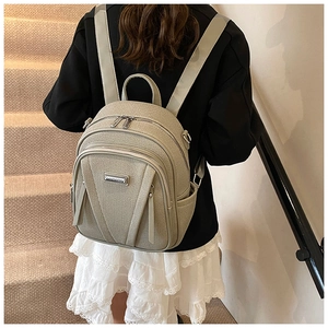 Close-up of khaki backpack showing textured fabric, multiple zip pockets and metal logo