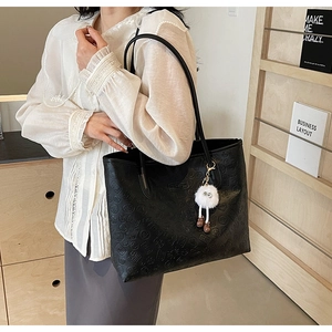 Detail of black embossed leather tote bag with unique stamp patterns and plush charm