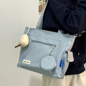 Detail of light blue nylon tote bag with small coin purse and plush charm on a model