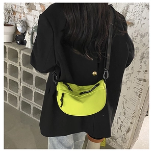 Detail of neon green nylon saddle bag with black strap worn by a model in a blazer