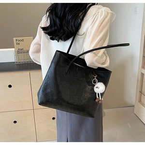 Close-up of black embossed tote bag with a cute white plush monster charm on the strap
