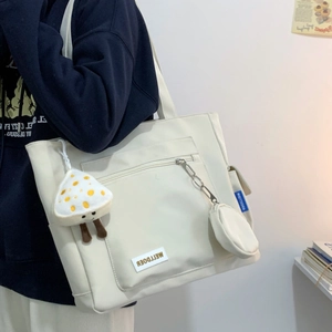 Detail of off-white tote bag with front zipper pocket and mushroom plush charm pendant