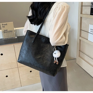 Detail of black tote bag with mahjong embossed pattern and cute plush doll charm