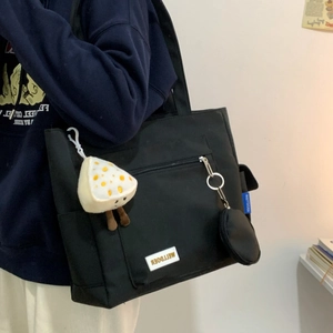 Close-up of minimalist black tote bag with plush cheese charm and logo detail