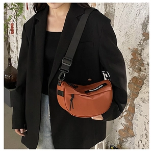 Close-up of caramel nylon saddle bag with wide strap on a model against a brick wall