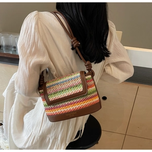 Detail of colorful woven crossbody bag with brown leather base and knot strap on a white dress