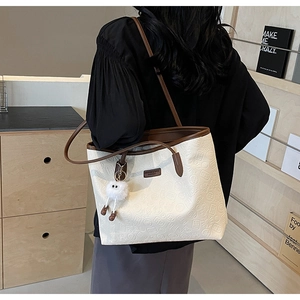 Detail of large beige tote bag featuring embossed patterns and brown leather straps