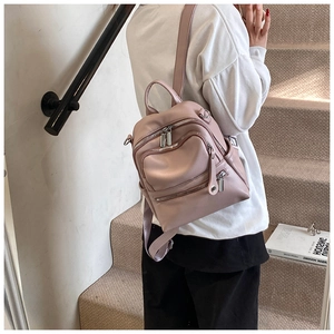 Detailed back view of a dusty pink faux leather backpack featuring multiple zip pockets