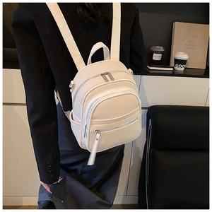 Detail of a creamy beige textured fabric backpack worn by a model in a cafe setting