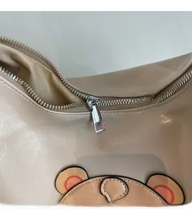 Macro detail of smooth silver zipper closure on stylish beige bag with bear pattern