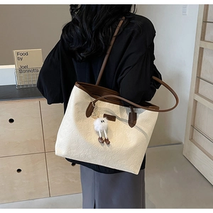 Detailed close-up of beige tote bag with embossed floral patterns and plush charm