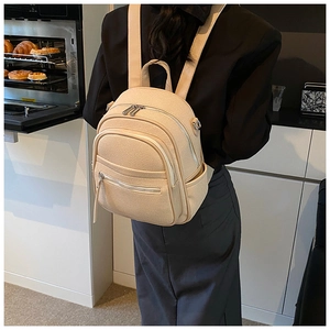 Detail of a beige multi-zipper backpack shown on model in a cozy kitchen setting