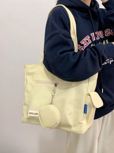Model wearing a beige nylon tote bag with functional pockets and a small coin purse