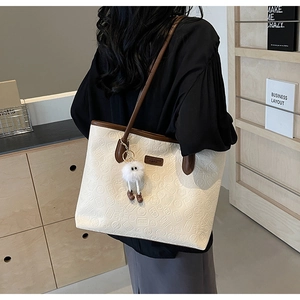 Detail of a large cream tote bag with embossed patterns and a brown shoulder strap