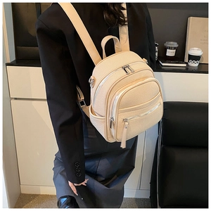 Close-up of beige lychee grain leather mini backpack with dual zipper pockets and top handle