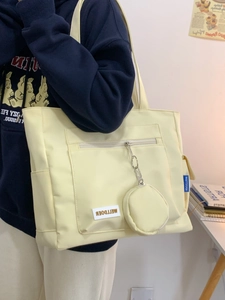 Detail of light yellow tote bag with round coin purse attachment and woven brand label