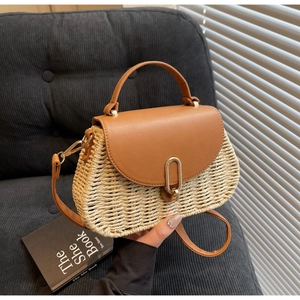 Detailed view of woven straw handbag featuring brown leather trim and golden U-shaped buckle