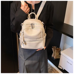 Detail view of cream white leather backpack showing lychee texture and multi-zipper compartments
