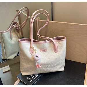 Detail of cream tote bag featuring embossed lotus patterns and a pink plush charm