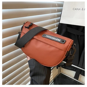 Macro detail of a burnt orange nylon saddle bag with a wide strap and fashion logo